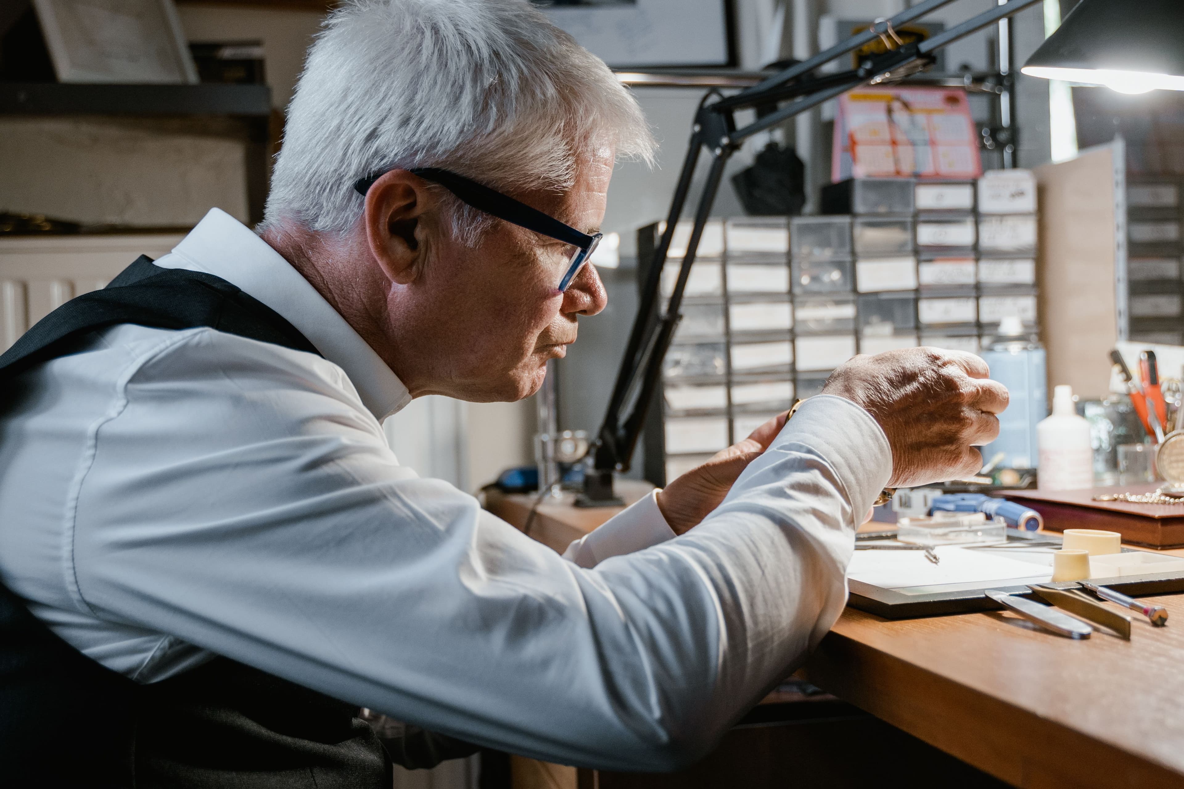An experienced watchmaker working at his bench under a desk lamp
